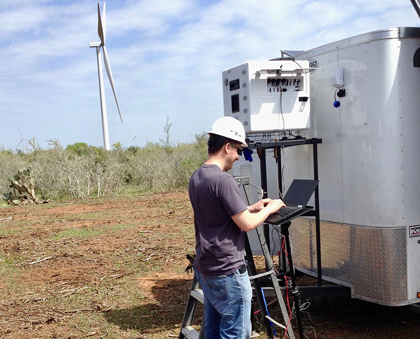 man checking performance of a wind turbine in the field from a laptop
