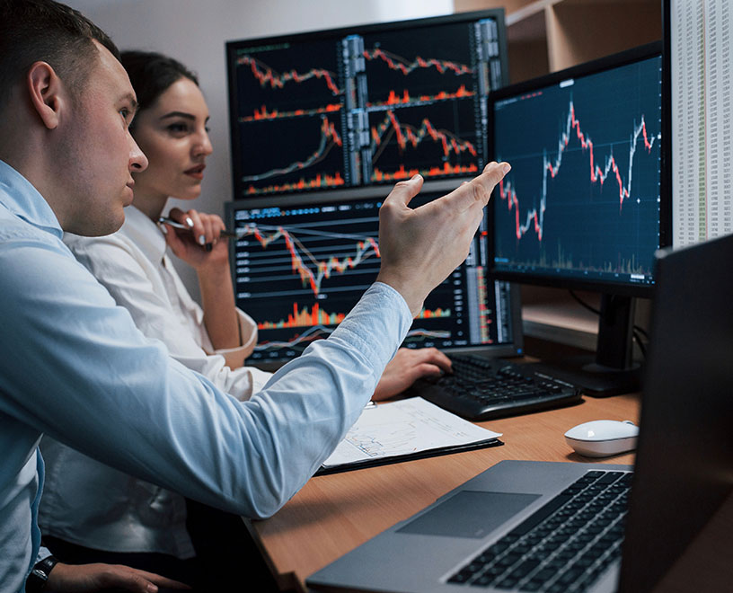 two colleagues discussing analytics in front of monitors displaying data two colleagues discussing analytics in front of monitors displaying data